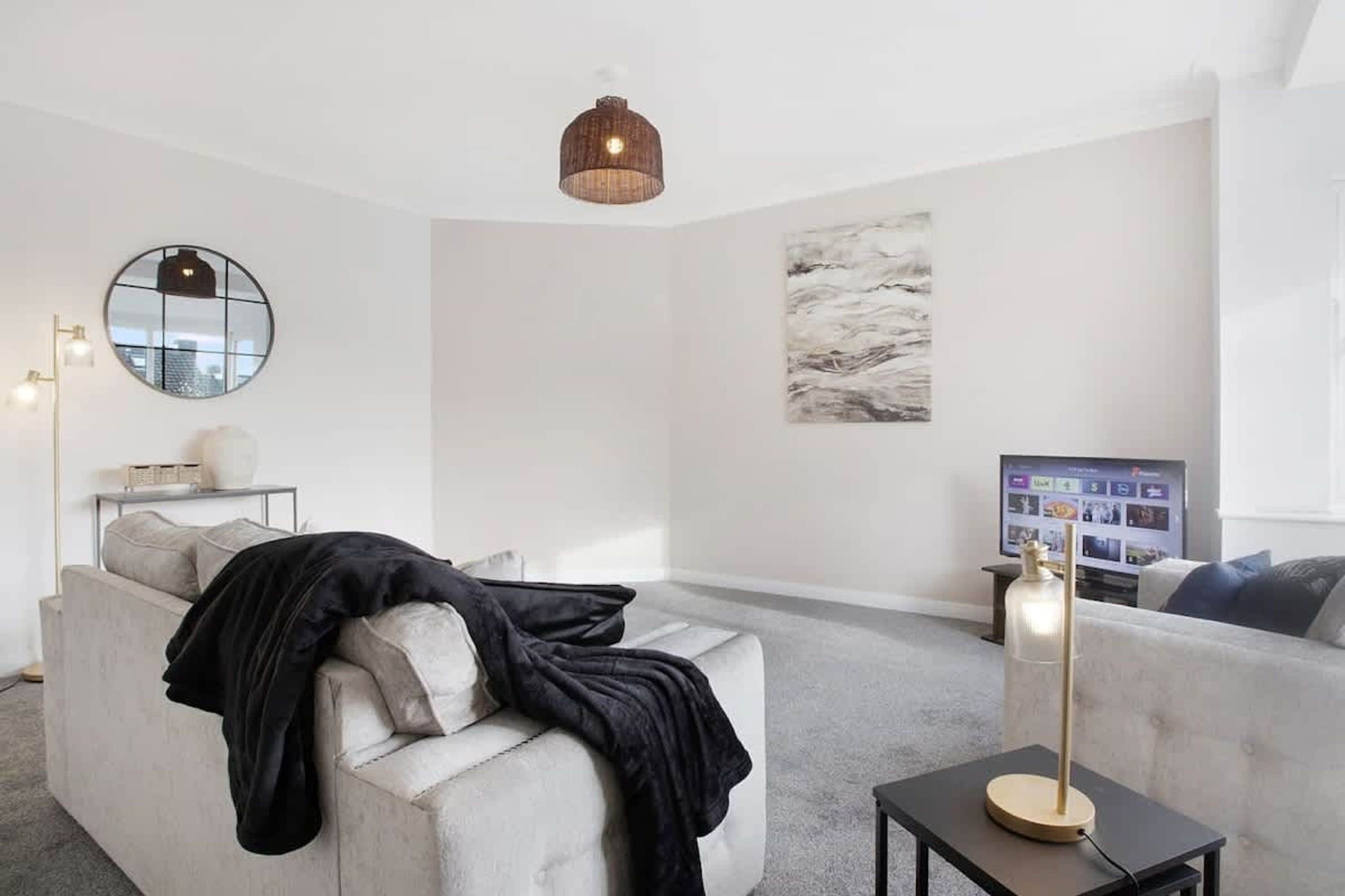 En moderne stue med sofa, sofabord, gulvlampe, rundt spejl og et billede på væggen.
