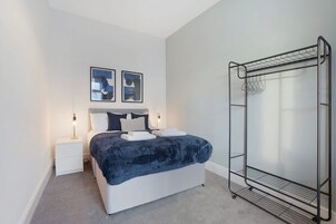 Un dormitorio con cama, dos mesitas de noche, una lámpara de pared y un tendedero de metal.