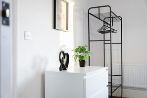 A white dresser with a black plant and a pair of scissors. A black metal shelf unit is against the wall. - Sunderland 3BR Retreat Sleeps 6 by Stay With Us (Sunderland)