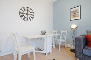 Ein modernes Wohnzimmer mit einem weißen Esstisch, Stühlen, einer Stehlampe und einer Wanduhr.