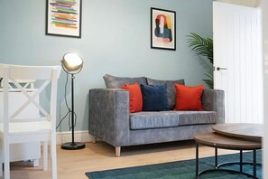 Ein Wohnzimmer mit grauem Sofa, rundem Couchtisch, Stehlampe und weißem Sessel.