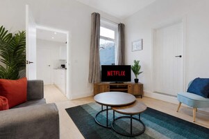 Una sala de estar moderna con una televisión de pantalla plana, un sofá gris, un sillón azul y una pequeña mesa de centro.
