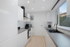 A modern kitchen with white cabinetry, a black countertop, a built-in oven, and a window providing a view of the outside. - Sunderland 3BR Retreat Sleeps 6 by Stay With Us (Sunderland)