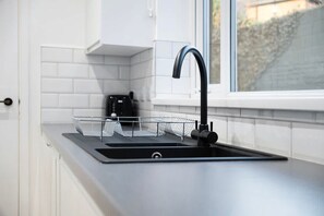 A modern kitchen with a black sink, white tiles, and a window with a view of a garden. - Sunderland 3BR Retreat Sleeps 6 by Stay With Us (Sunderland)