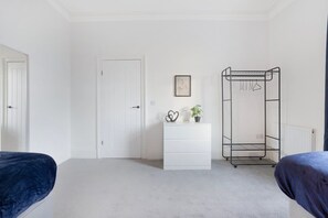A bedroom with two beds, a white door, a white dresser, a metal drying rack, and a framed picture on the wall. - Sunderland 3BR Retreat Sleeps 6 by Stay With Us (Sunderland)