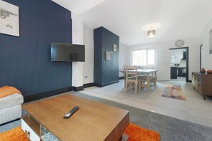A modern living room with a flat-screen TV, a dining area with a table and chairs, and a kitchen visible through an open door. - 5BR Sleeps 10 Perfect for Contractors in Durham (Durham)