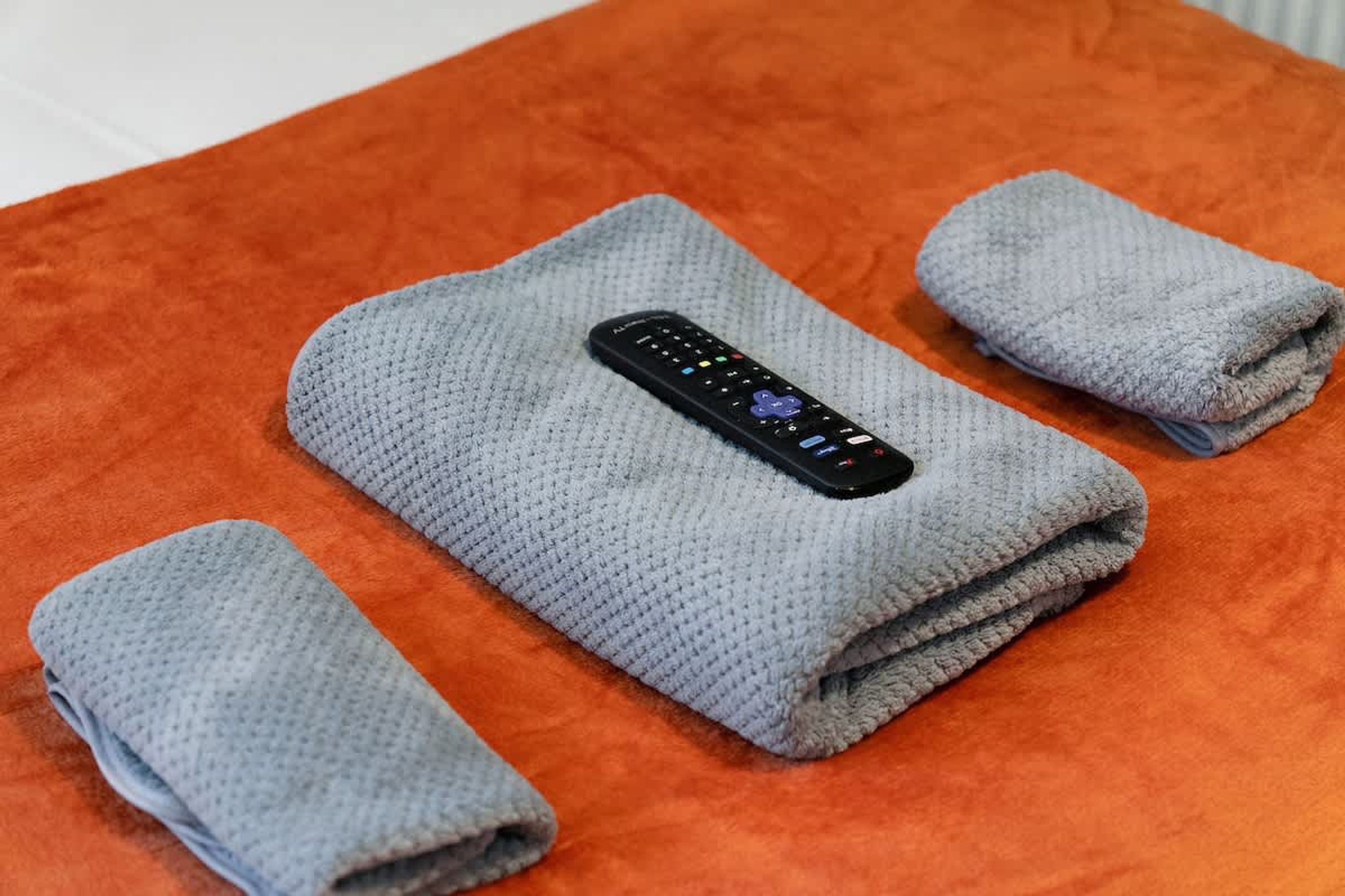 A folded towel and a remote control on an orange surface.