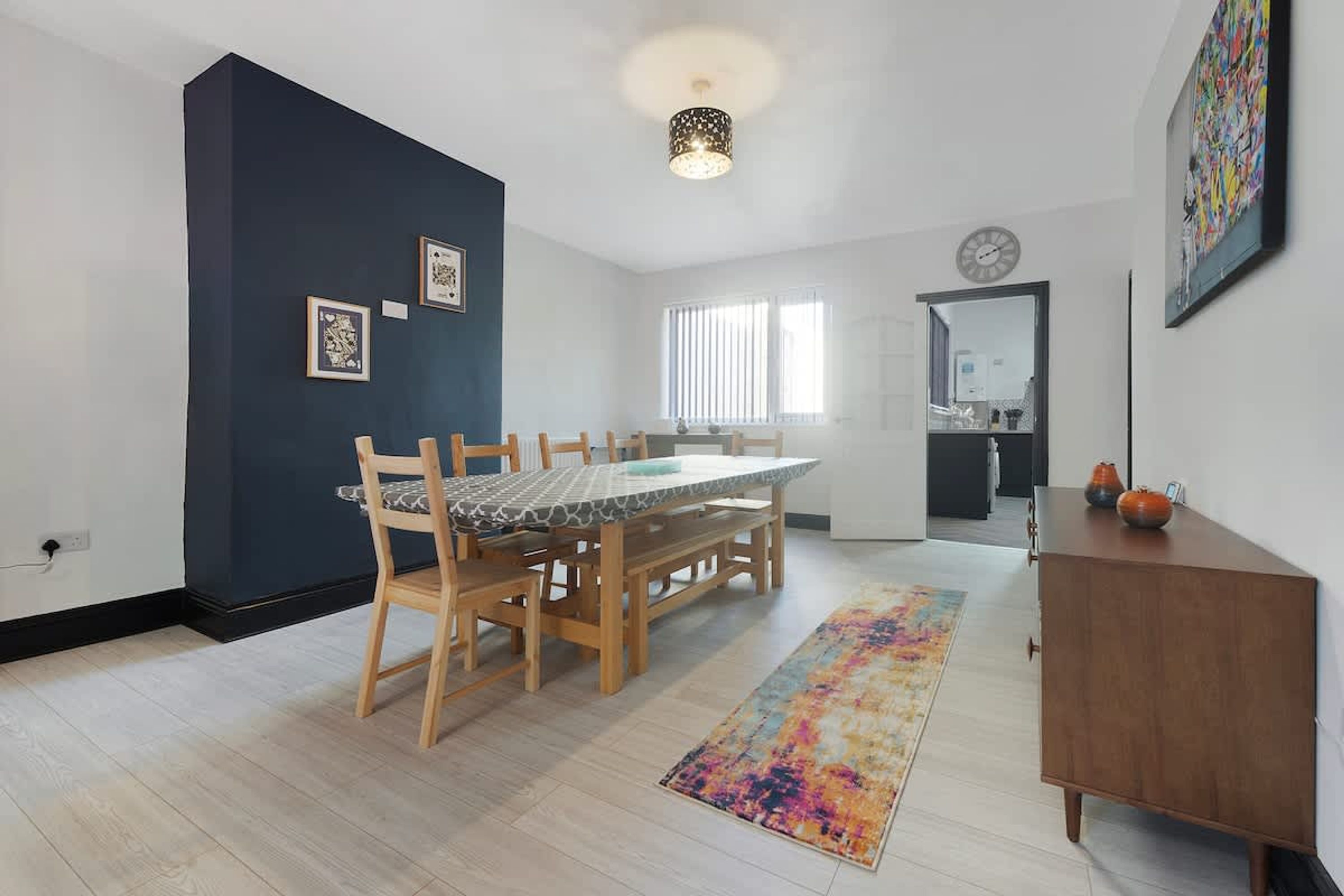 A dining area with a table and chairs, a rug, a cabinet, and a wall with framed pictures.
