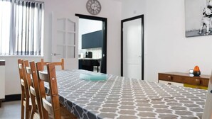 A dining area with a table set for four, wooden chairs, a patterned tablecloth, a clock on the wall, and a kitchen visible through an open door. - 5BR Sleeps 10 Perfect for Contractors in Durham (Durham)