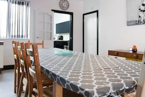 A dining area with a table set for four, wooden chairs, a patterned tablecloth, a clock on the wall, and a kitchen visible through an open door. - 5BR Sleeps 10 Perfect for Contractors in Durham (Durham)