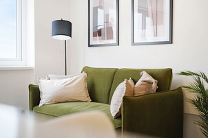 Un sofá verde con almohadas blancas, una lámpara de pie y cuadros en la pared.