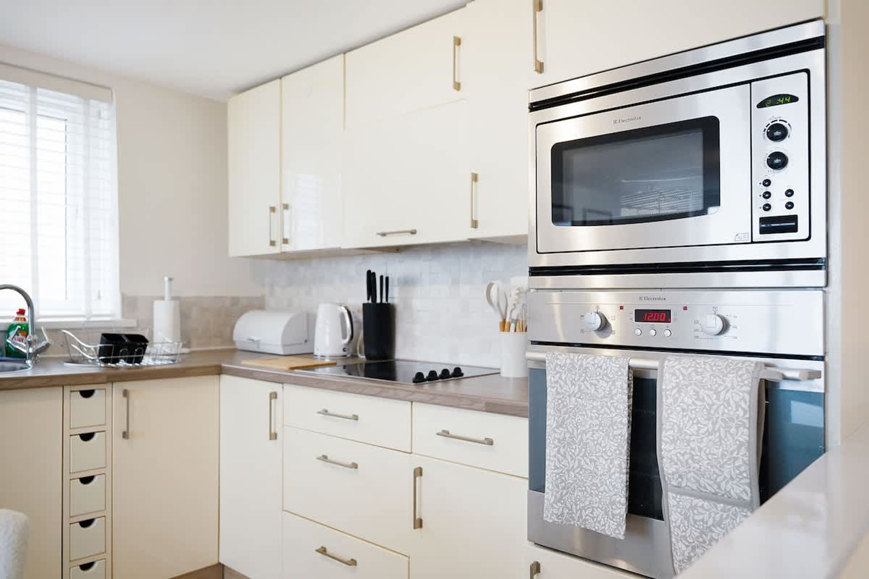 A modern kitchen with white cabinetry, a stainless steel microwave, a built-in oven, and a coffee maker.