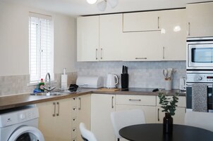 Una cocina moderna con armarios blancos, horno empotrado, microondas y cafetera.