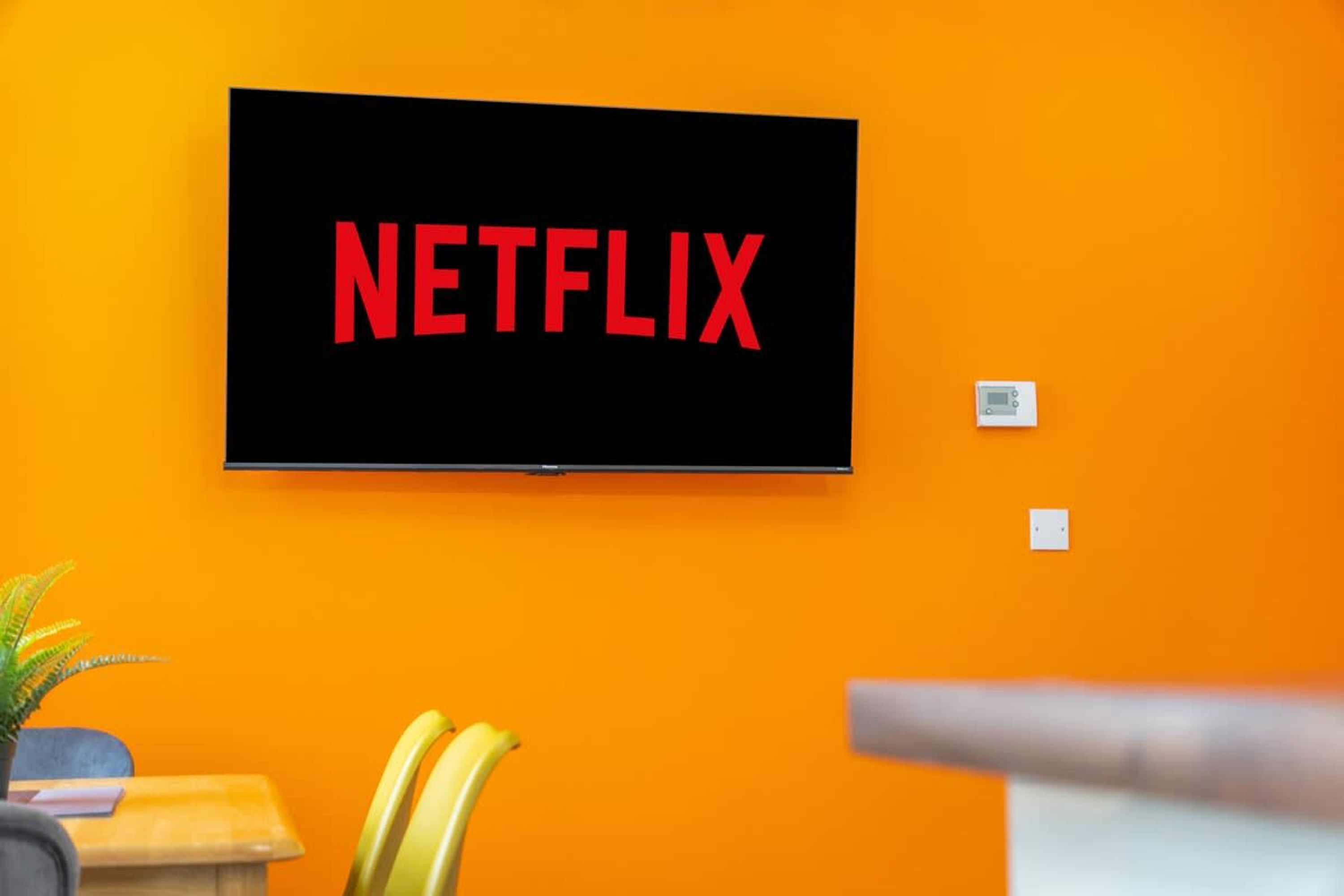 A television mounted on an orange wall displaying the Netflix logo.
