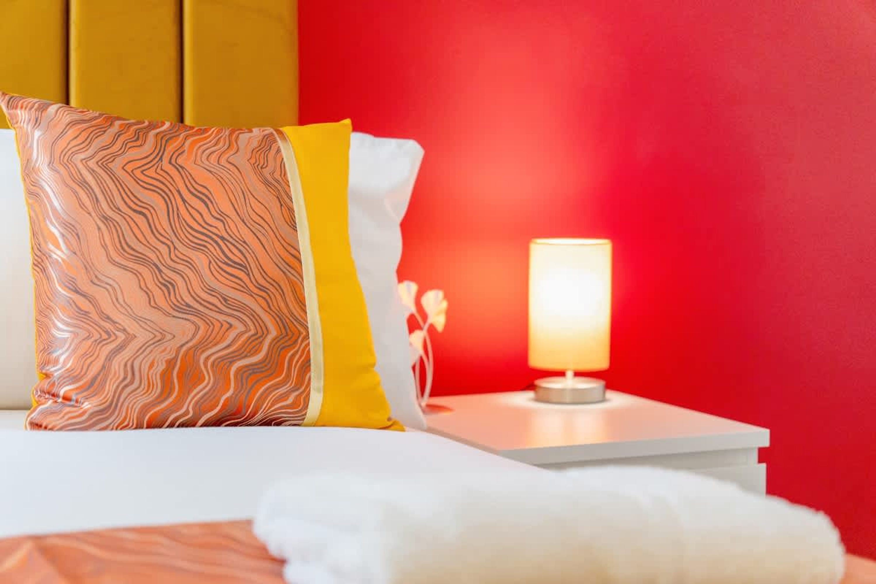 Un lit avec un oreiller à motifs, une table de chevet avec une lampe et un mur rouge.