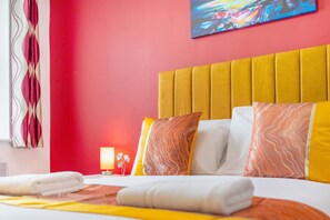 Une chambre d’hôtel avec un mur rouge vif, une tête de lit jaune et des coussins à motifs.