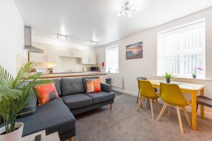Ein modernes Wohnzimmer mit einer Couch, einem Esstisch mit Stühlen, einer Küche im Hintergrund und einem großen Fenster mit Blick.
