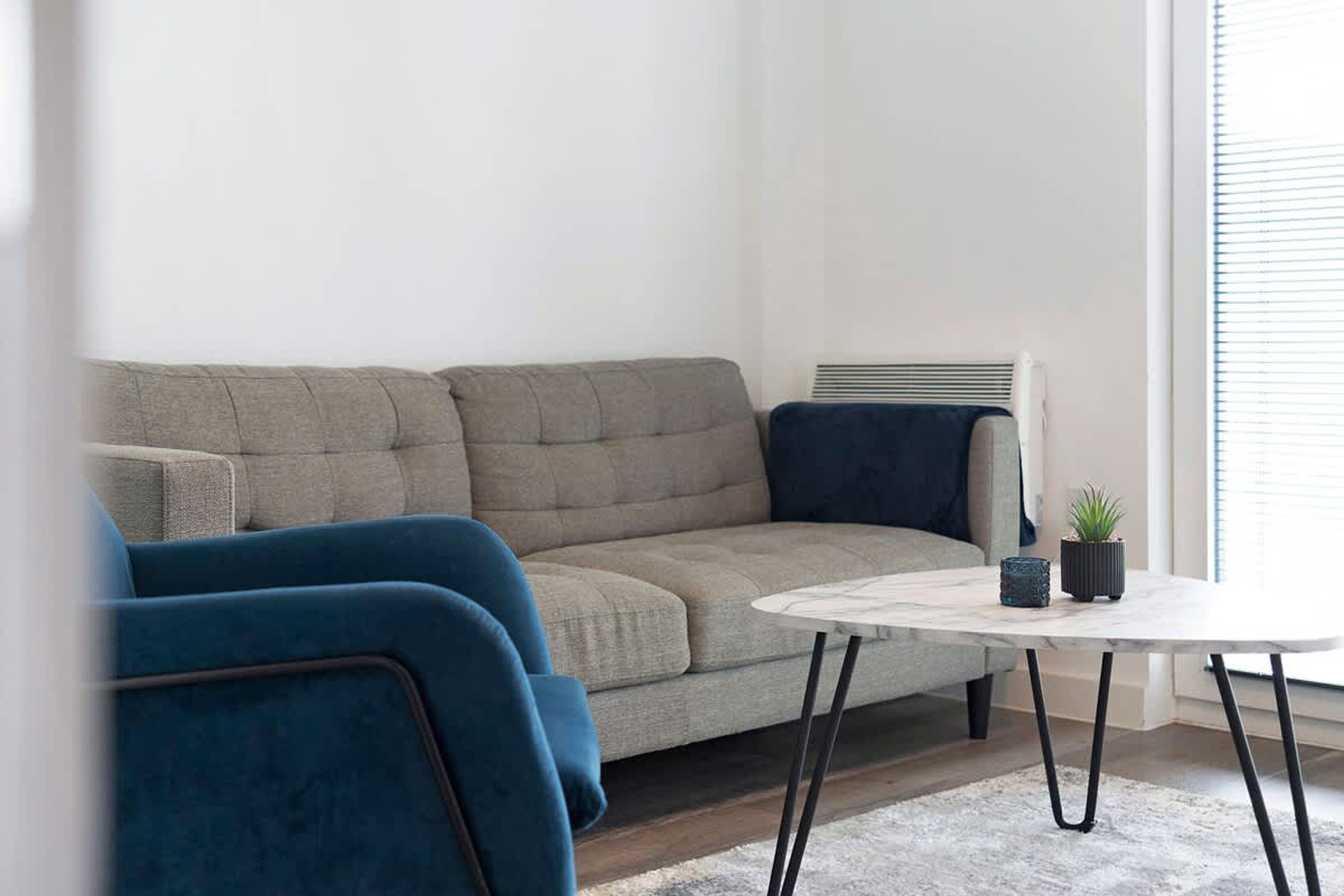 A living room with a sofa, a blue armchair, a small round table, and a potted plant.