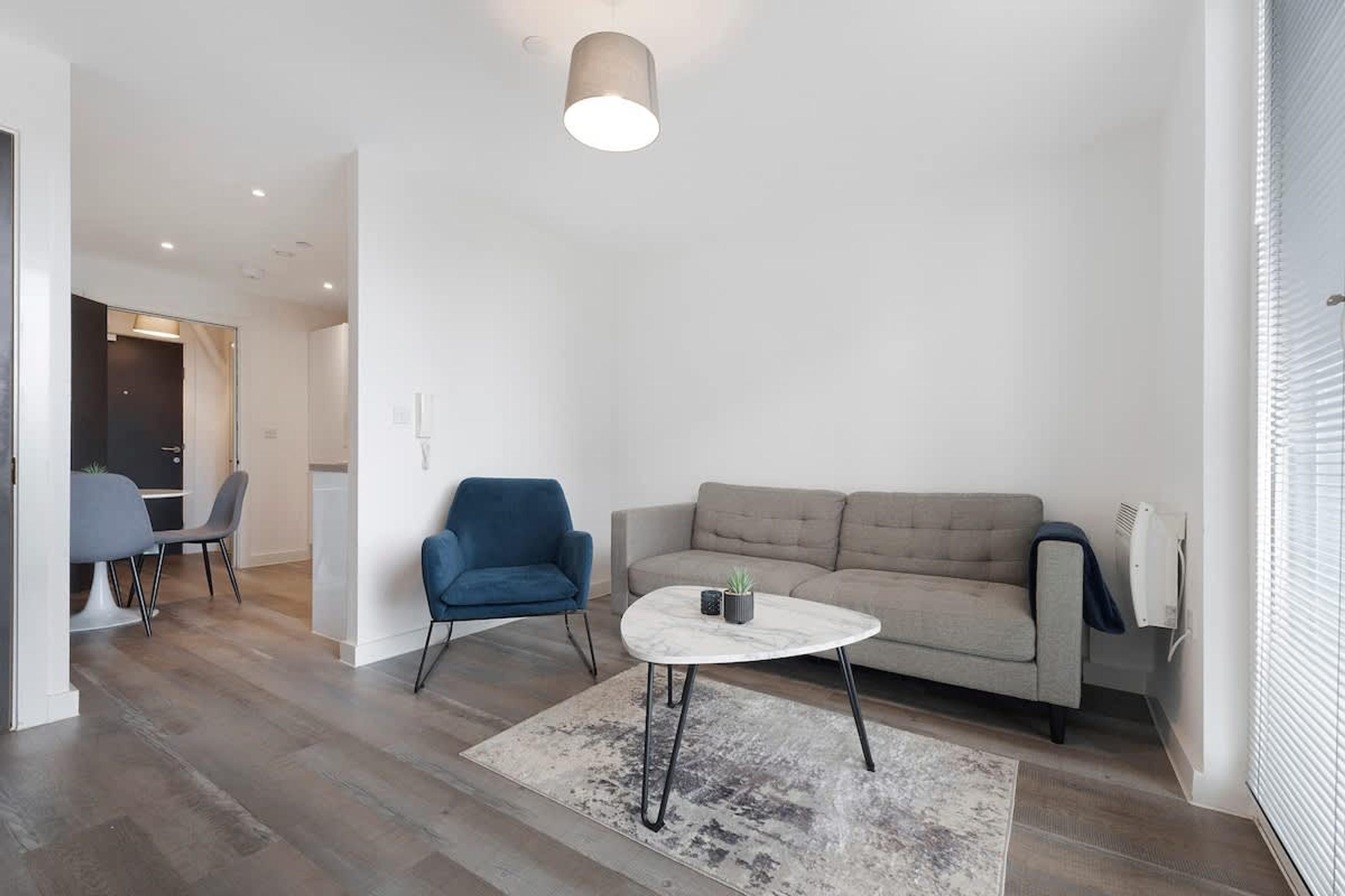 Una sala de estar moderna con un sofá gris, un sillón azul, una mesa de centro redonda y un tapete estampado.