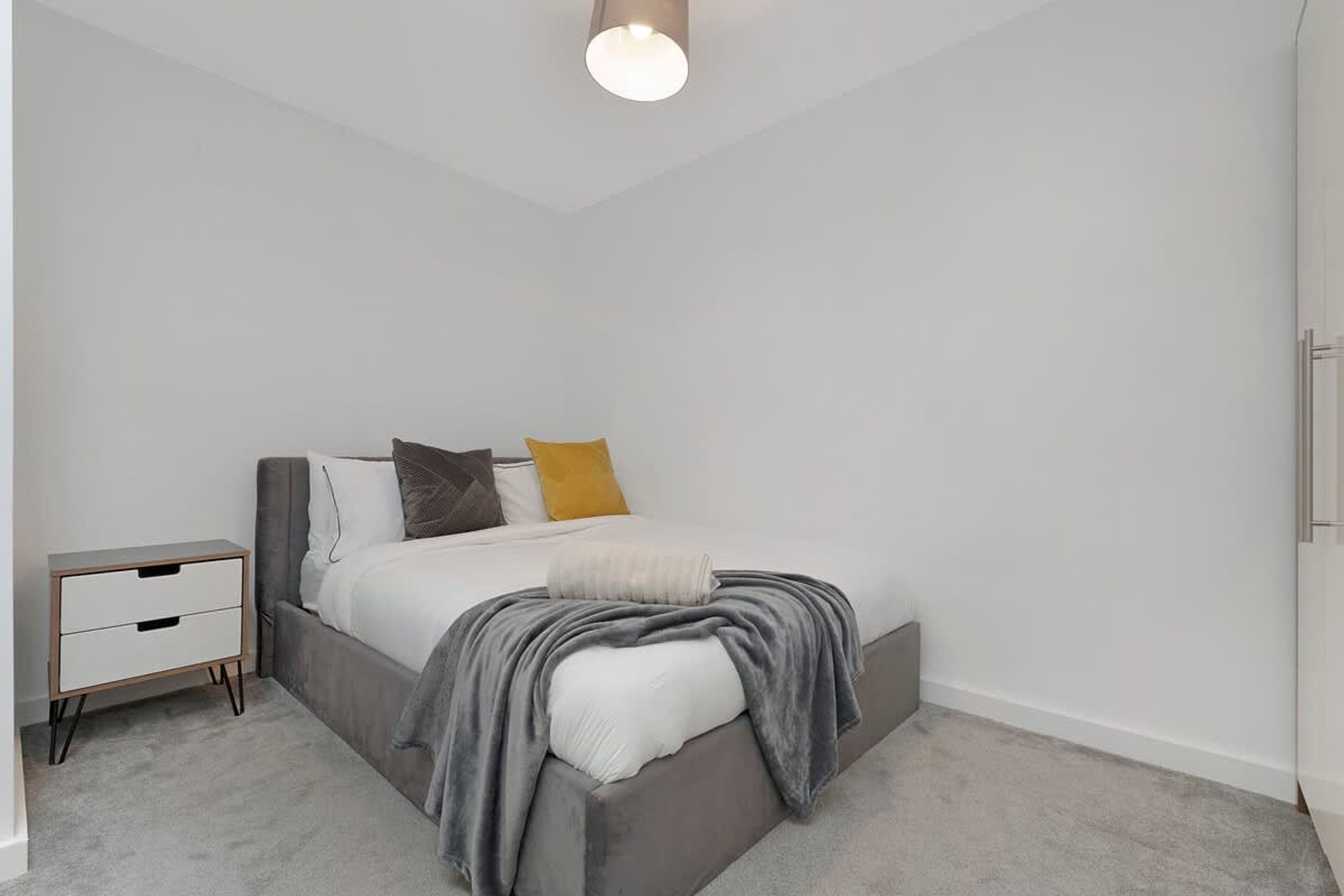 A bedroom with a bed, bedside table, and a hanging light fixture.