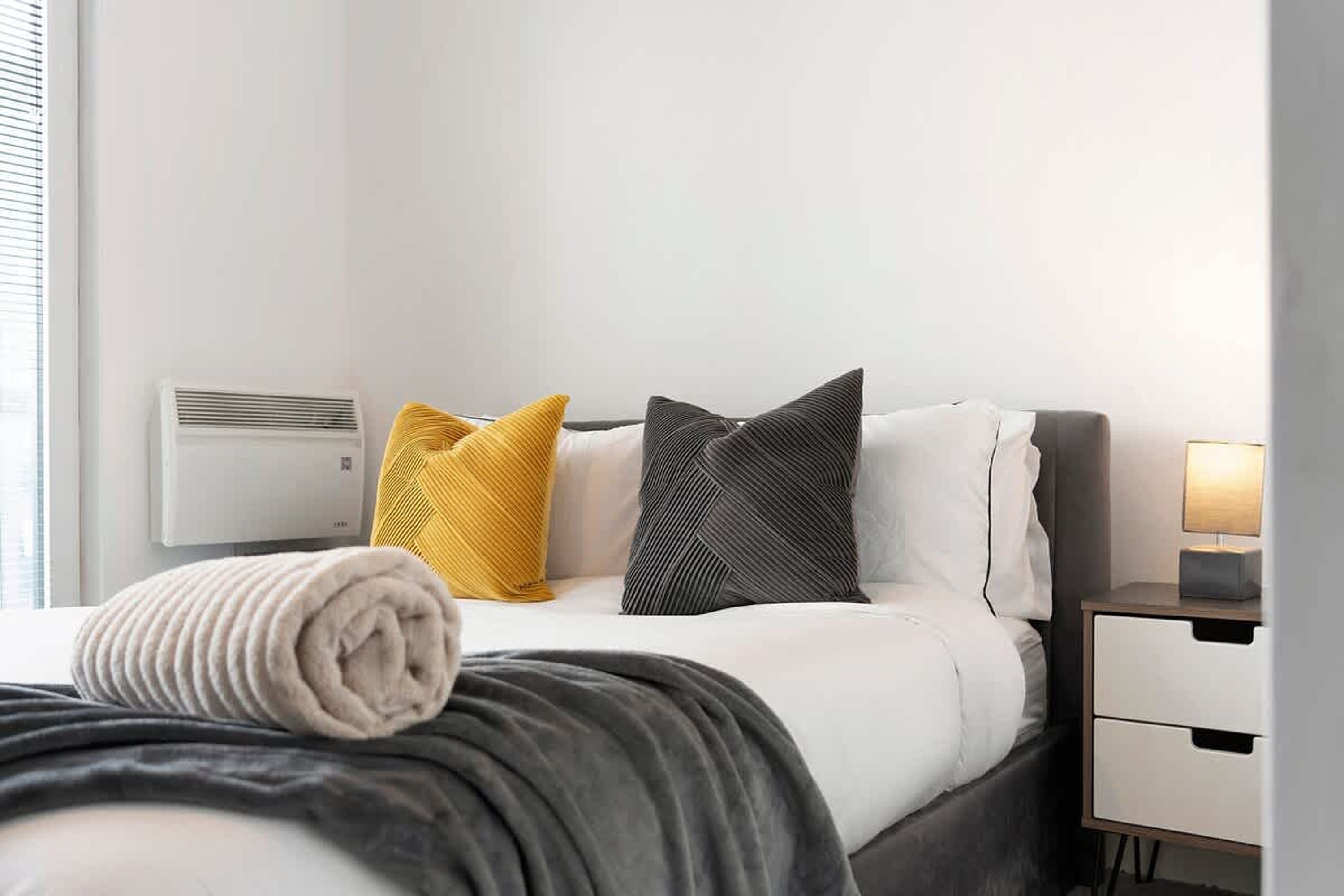Una habitación de hotel con una cama, una mesita de noche con lámpara y un aire acondicionado instalado en la pared.