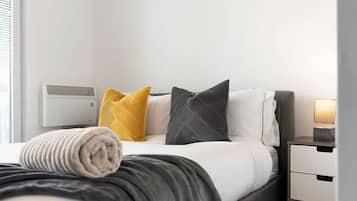 Una habitación de hotel con una cama, una mesita de noche con lámpara y un aire acondicionado instalado en la pared.