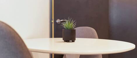Una mesa redonda blanca con una planta en maceta en el centro, una puerta con picaporte y una silla con cojín oscuro.