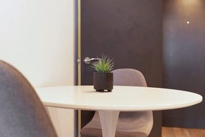 Een ronde witte tafel met een kamerplant in het midden, een deur met een handgreep, en een stoel met een donkere kussen.