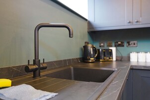 Una cocina con un grifo moderno, una cafetera y una tetera sobre la encimera.