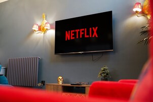 Una sala de estar moderna con un televisor de pantalla plana grande montado en la pared que muestra 'NETFLIX' en letras rojas, un radiador, una mesita con una decoración de calavera y una planta en maceta.