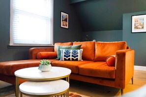 A room with a sectional sofa, a small round table, and a potted plant. - Central Hartlepool 2BR Retreat Sleeps 3 by Stay With Us (Hartlepool)
