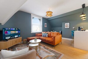 A modern living room with a television, sofa, coffee table, and a kitchen area with a bar. - Central Hartlepool 2BR Retreat Sleeps 3 by Stay With Us (Hartlepool)