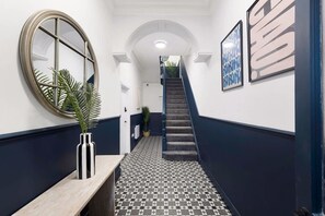 Ein Flur mit Schachbrettmuster, einem runden Spiegel und einer Treppe, die in eine obere Ebene führt.