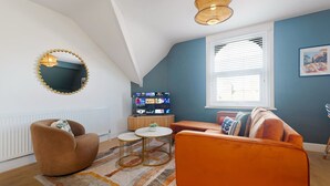 Moderni olohuone, jossa on kalteva katto, televisio, pyöreä sohvapöytä ja sohva.