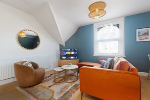 A modern living room with a sloped ceiling, a television, a round coffee table, and a sofa. - Central Hartlepool 2BR Retreat Sleeps 3 by Stay With Us (Hartlepool)