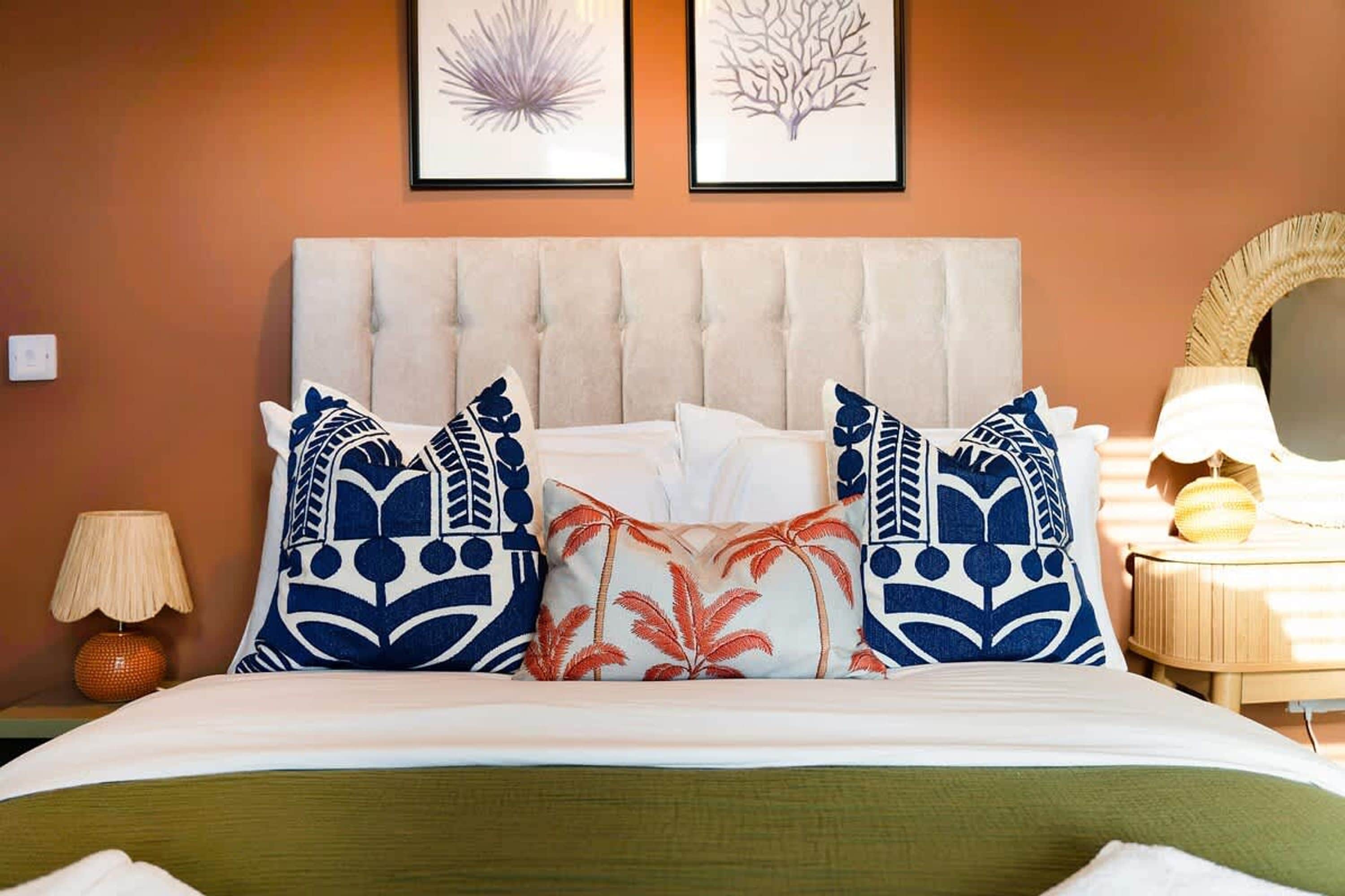 A hotel room with a tufted headboard, a bed with white bedding, and decorative pillows. There are two framed wall art pieces above the bed.