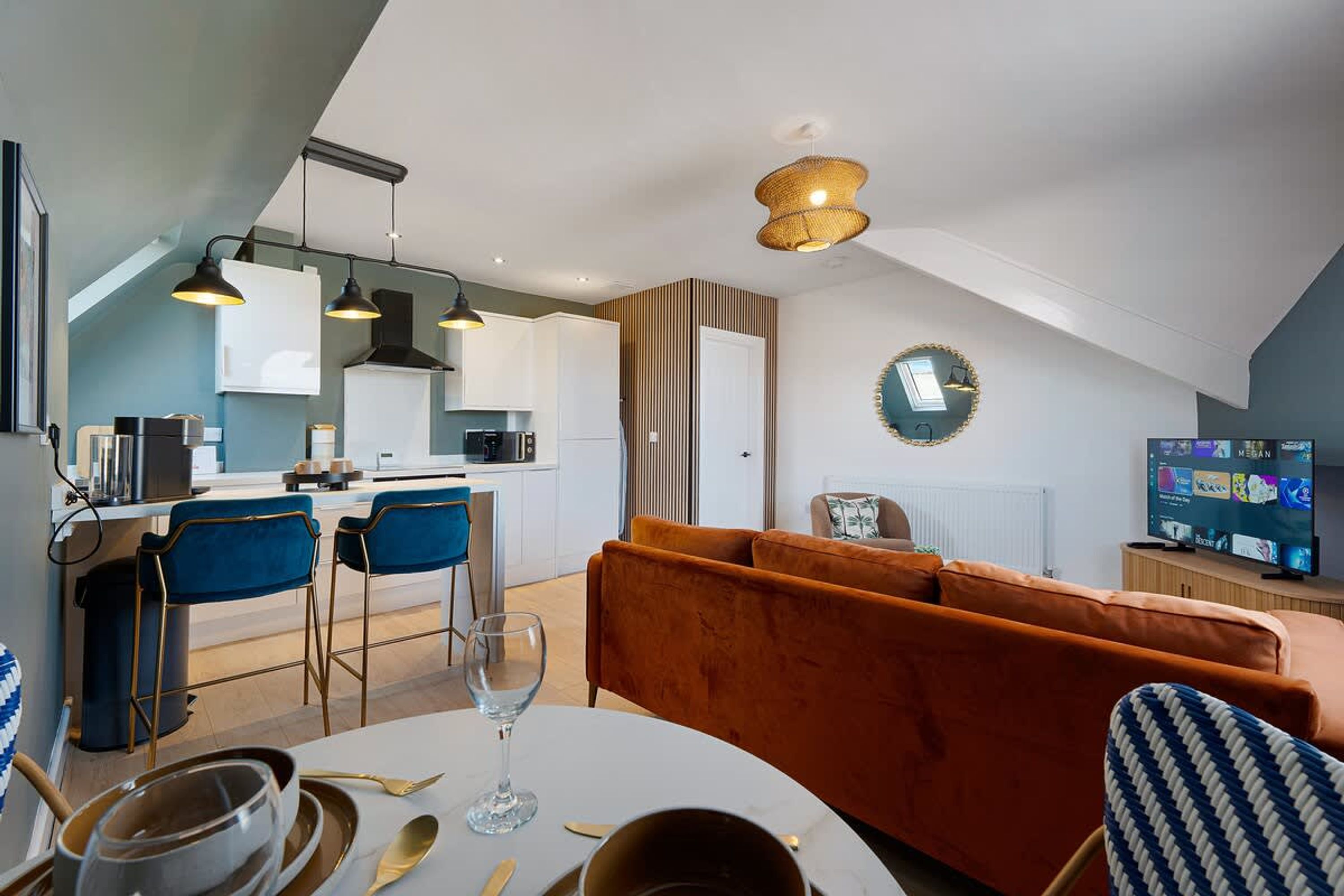A modern kitchen with a dining area, a living room with a sofa, and a television.