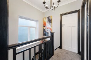 Ein Flur mit Fenster, einem Gemälde, einer Tür und einer Treppe.
