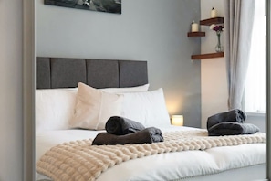 A neatly made bed with white linens and two rolled towels, a grey headboard, and a bedside table with a vase of flowers. - 3BR in Baxter Avenue With Netflix Wifi Backyard (Newcastle-upon-Tyne)