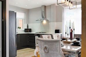 A modern kitchen with dark cabinetry, a stainless steel range hood, and a dining area with a marble countertop and a tufted chair. - 3BR in Baxter Avenue With Netflix Wifi Backyard (Newcastle-upon-Tyne)