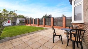 A patio with a table and chairs, a brick wall, and a grassy lawn. - 3BR in Baxter Avenue With Netflix Wifi Backyard (Newcastle-upon-Tyne)