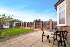 A patio with a table and chairs, a brick wall, and a grassy lawn. - 3BR in Baxter Avenue With Netflix Wifi Backyard (Newcastle-upon-Tyne)