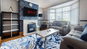 A living room with a fireplace, a sofa, a coffee table, and a TV mounted above the fireplace displaying the Netflix logo. - 3BR in Baxter Avenue With Netflix Wifi Backyard (Newcastle-upon-Tyne)