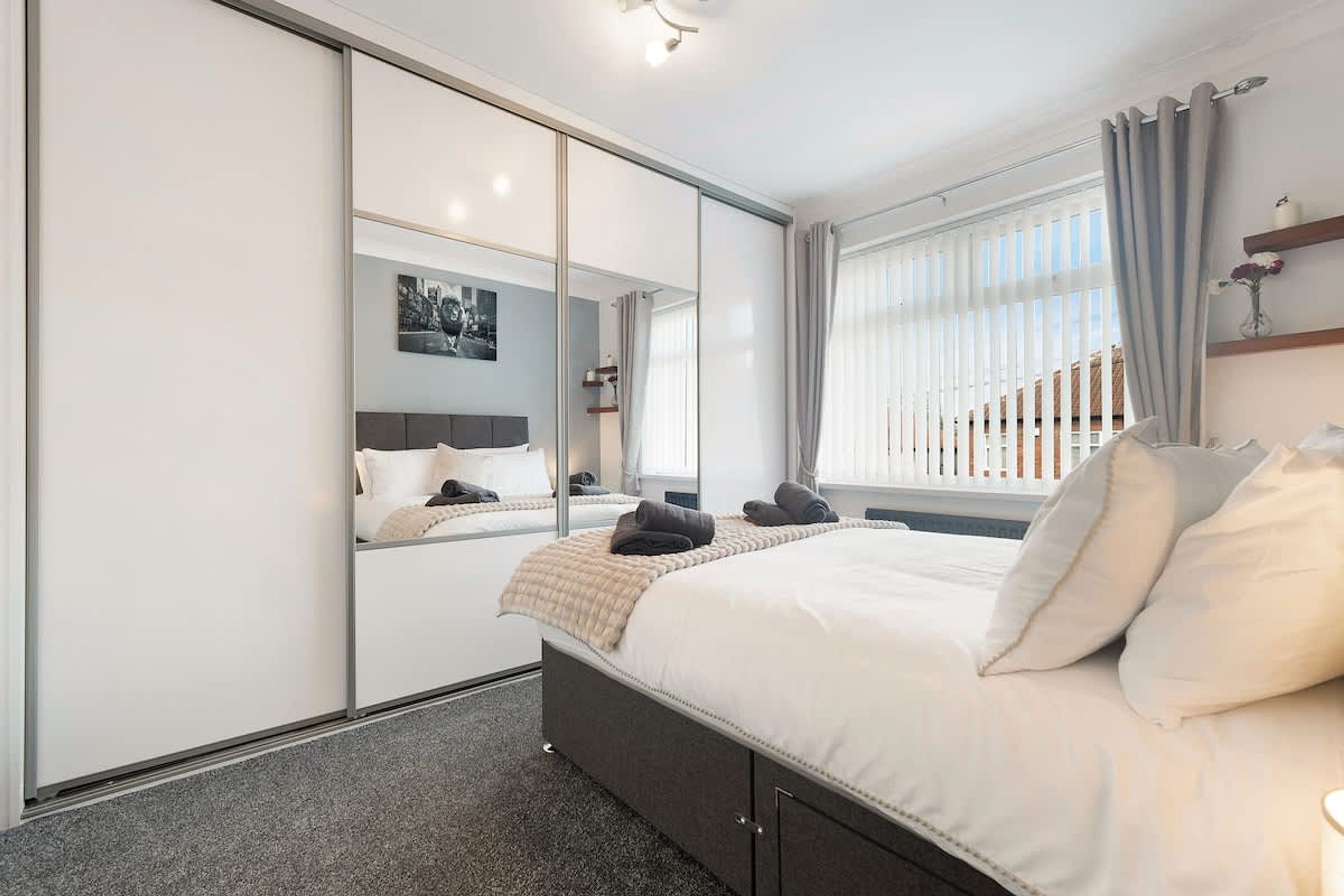 A modern bedroom with a large bed, a mirror, and a window with curtains.