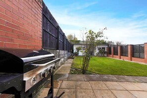 Ein Grill mit einem Backsteinwall und einem Holenzaun im Hintergrund.