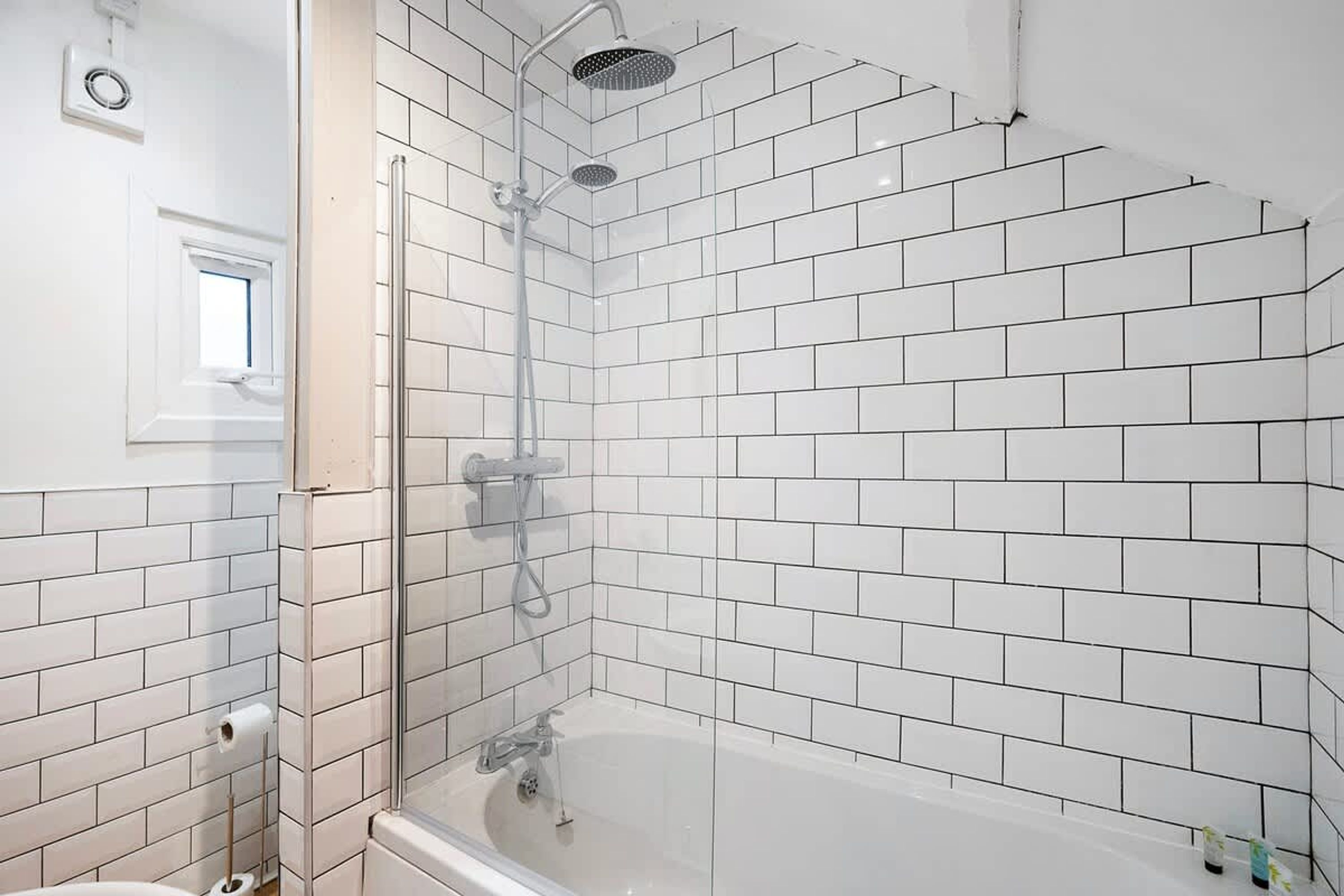 Un baño con azulejos blancos tipo metro, ducha con mampara de vidrio y bañera.
