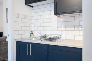 Una cocina con salpicadero de azulejos blancos, armarios azul oscuro, un lavamanos de acero inoxidable y un escurreplatos.