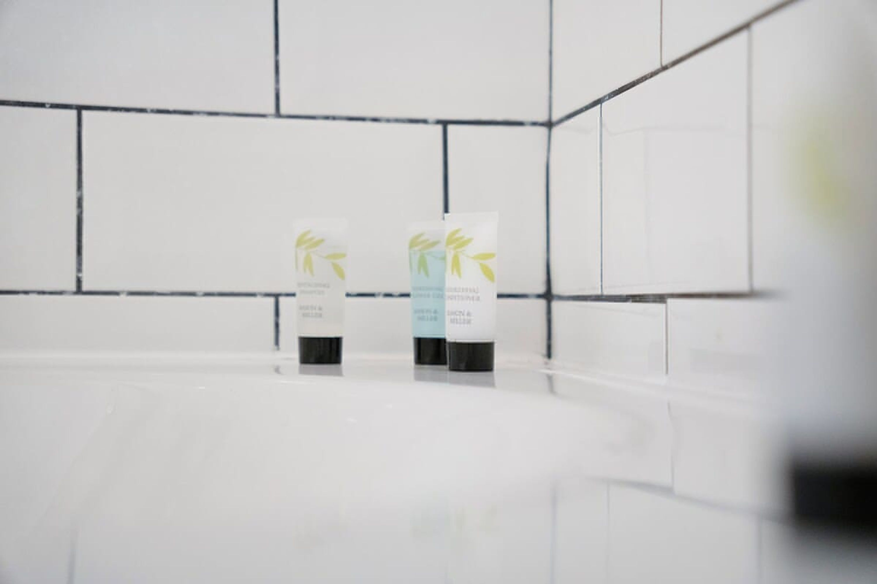 Ein helles, modernes Badezimmer mit weißen Fliesen und zwei weißen Spenderstationen mit Blattform-Design.