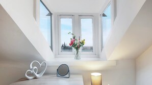 Ein Zimmer mit Dachfenster, einem Nachttisch mit Lampe und einer Vase mit Blumen.