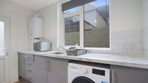 A modern kitchen with a built-in washing machine, a window with a view of the outside, and a countertop with a kettle and toaster. - Seaside Haven on Newcomen Grove Redcar Retreat (Redcar)